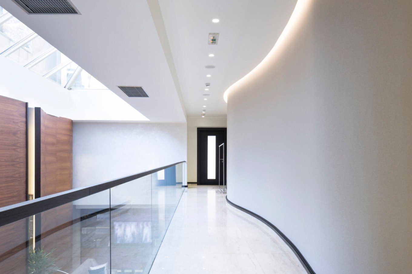 Curved plaster wall and glass balustrade along a hallway